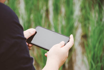 Cropped hands of man using mobile phone on field