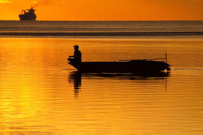 Silhouette man in boat on sea against orange sky