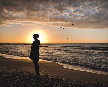 Silhouette man standing on beach against sky during sunset