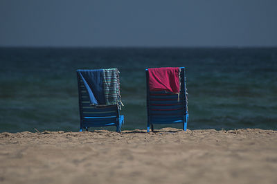 Lounge chairs on beach against clear blue sky