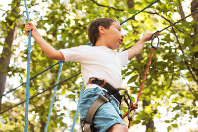 Low angle view of boy on obstacle course in forest