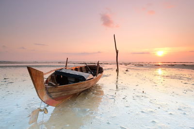 Boat moored on beach against sky during sunset