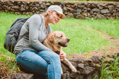 A girl with a backpack is sitting on the lawn hugging a labrador retriever and smiling. outdoor 