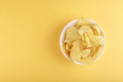 Crispy potato chips in bowl on yellow background, top view