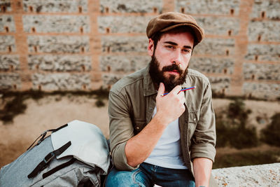 Man with backpack holding pencil and book while sitting outdoors