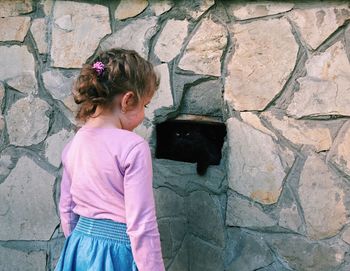 Girl standing by cat on brick wall