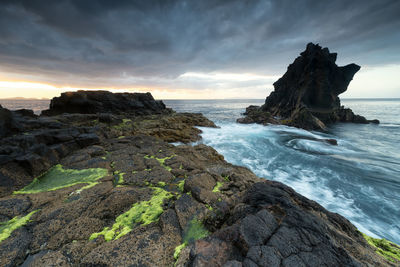 Rock formation on beach against sky during sunset