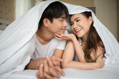 Happy couple under blanket in bedroom at home