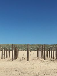 Wooden posts on sand against clear blue sky