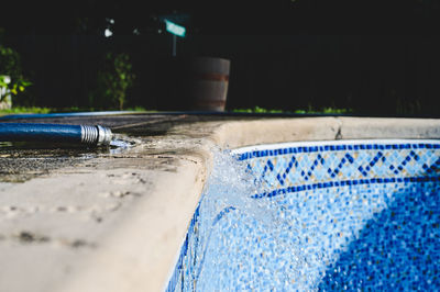 Close-up of water hose filling a swimming pool in the daytime