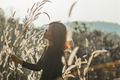 Side view of woman with plants on field against sky