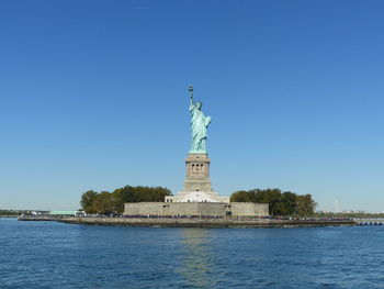 Statue of liberty by hudson river against clear blue sky