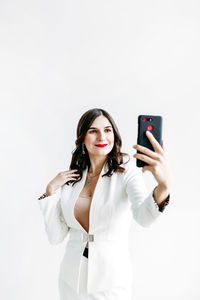 Young woman using phone while standing against white background