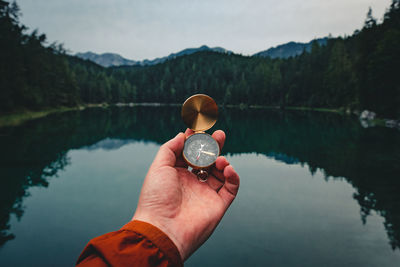 Cropped hand holding compass against lake in forest