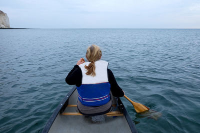 Rear view of woman rowing boat in sea against sky