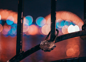 Close-up of padlock hanging on railing against illuminated lights