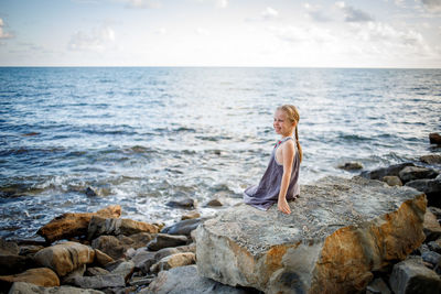 Woman standing on rock in sea against sky