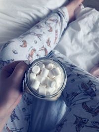 Low section of woman holding jar with marshmallows on bed at home