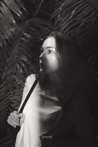 Thoughtful woman looking away while standing against plants at night