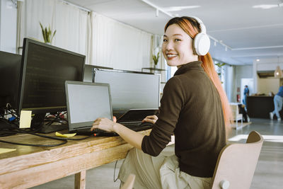 Portrait of smiling female programmer working on laptop in creative office