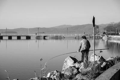 Man standing on rock by lake against clear sky