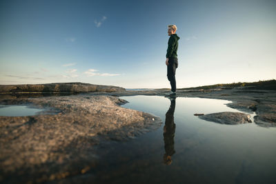 Woman standing on coast and reflecting in puddle