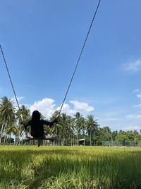 Rear view of woman on field against blue sky