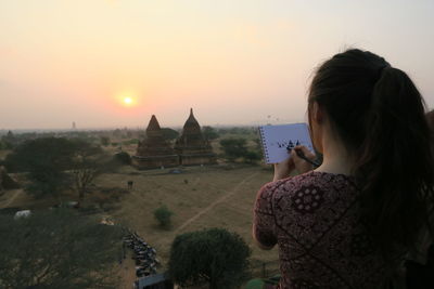 Rear view of woman photographing cathedral against sunset sky