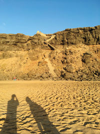 Shadow of people on sand dune against clear sky