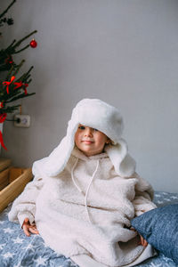 Cute child y on the bed in cozy adult clothes and a hat with earflaps.