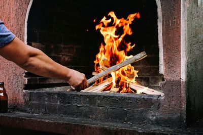 Midsection of man holding burning fire on wood on barbecue grill