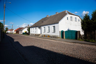 Road by houses against clear blue sky