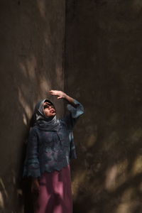 Young woman wearing hijab standing by wall