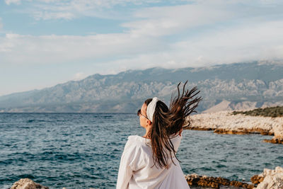 Rear view of young woman in white shirt standing on beach. sea, summer, view, lifestyle.