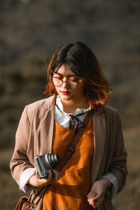 Young woman holding camera while standing outdoors