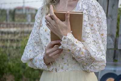 Mid section of woman holding book standing outdoors