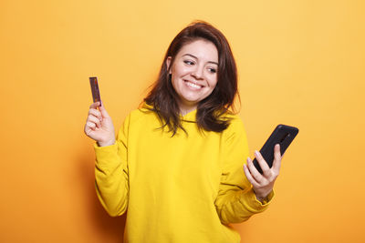 Young woman using mobile phone against yellow background