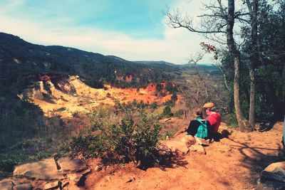 Couple sitting on mountain against sky during sunny day