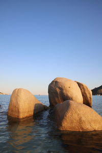 Rocks in sea against clear blue sky