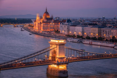 Illuminated bridge over river in city against sky at night