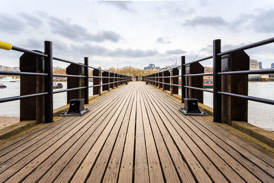 Pier on footbridge over river against sky