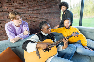 Young man playing guitar while sitting on sofa at home