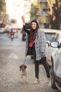 Smiling woman hailing ride while standing with dog on street in city