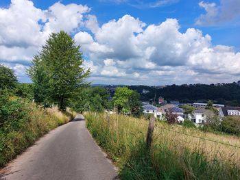 Road amidst trees and buildings against sky