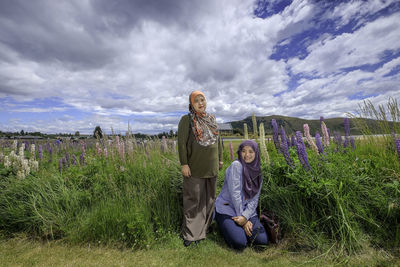 Mother with daughter on grassy field against cloudy sky