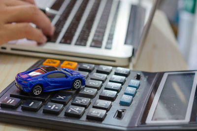 Close-up of toy car over calculator by person using laptop on table