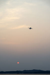 Low angle view of airplane flying over sea during sunset