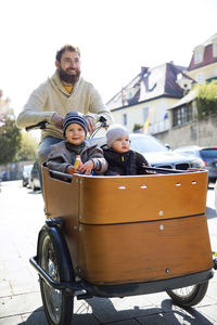 Happy father with two children riding cargo bike in the city