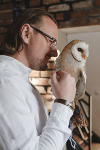 Man with owl at home. unusual pets and human animal friendship relationships. wild bird on hand