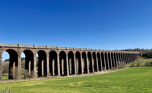 Arch bridge on field against clear blue sky